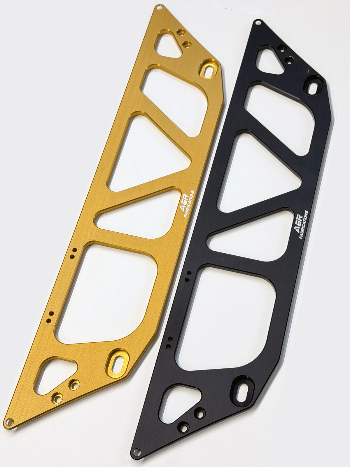 Two aluminum subframe braces, one in gold anodized finish and the other in black, displayed diagonally on a light gray background. Both feature triangular cutouts and the white 'AGR Fabrications' logo printed on them.
