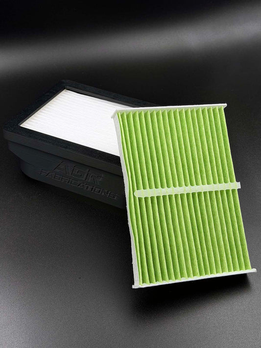 A green pleated car air filter with a black plastic tab closure, shown in front of its black packaging box on a dark gray background.