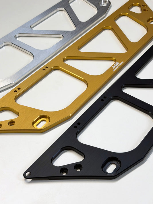 Three aluminum braces components in raw AL , gold, and black anodization options, arranged diagonally on a clean white background. The gold piece features a small white printed logo that reads "AGR Fabrications"